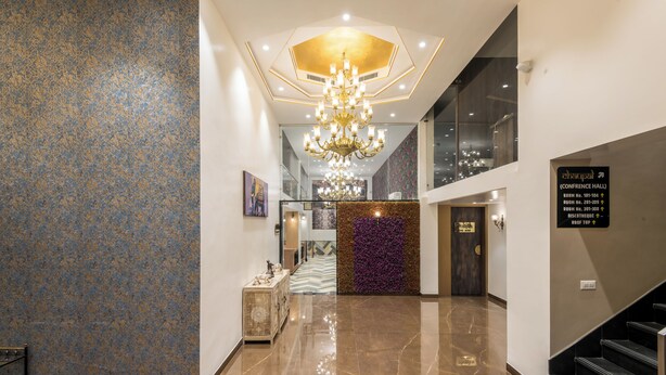Un hall d'hôtel moderne avec un lustre, un escalier et une enseigne indiquant l'accès à la salle de conférence.