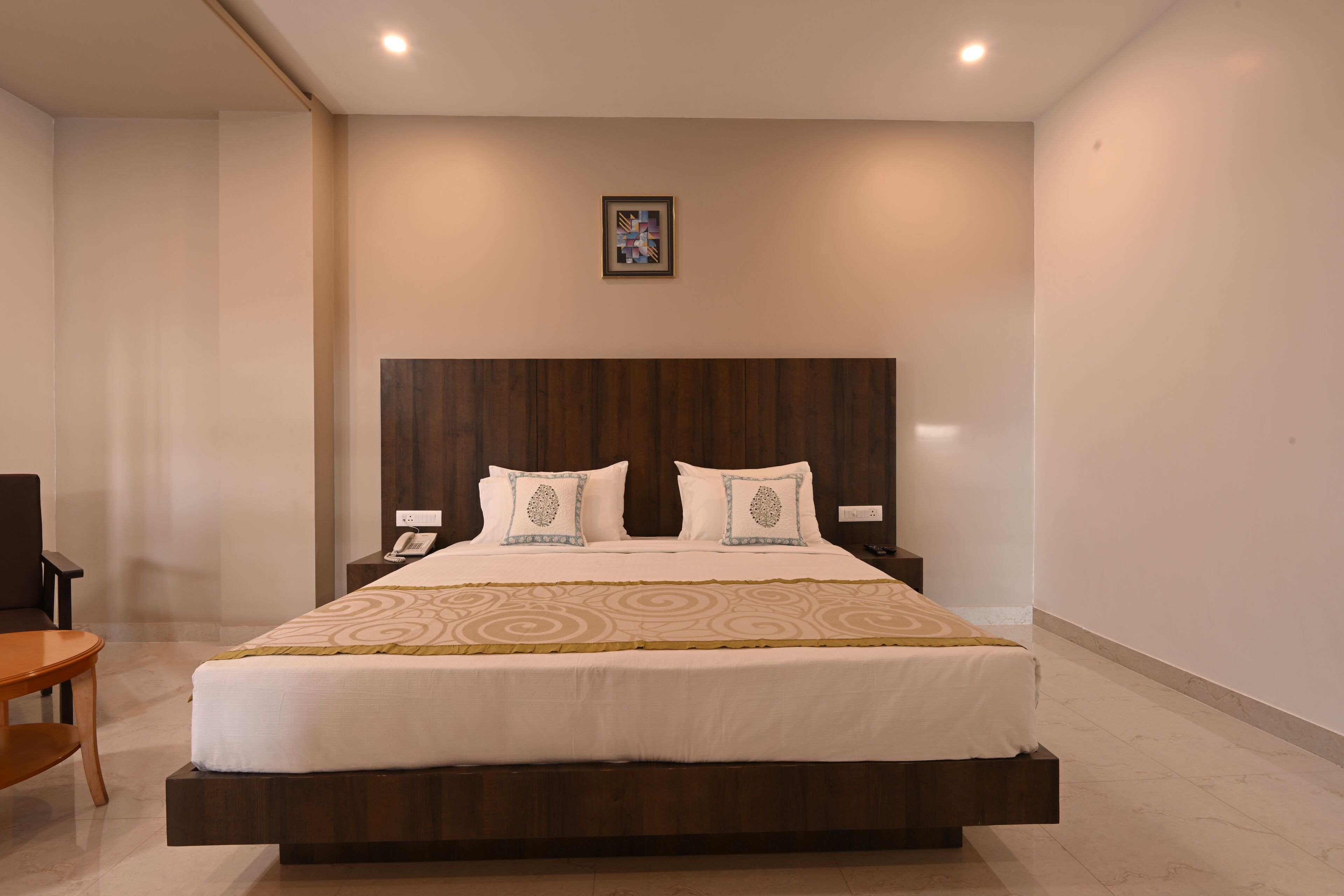 Una habitación de hotel moderna con una cama grande, cabecera de madera y una mesita de noche con un teléfono.