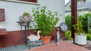 A building entrance with a white wall, a window, a small table with a plant and a stone sculpture, a potted plant, a metal sign, and a wooden duck sculpture. - Apartment in Bad Wunnenberg Near Ski Willingen (Bad Wuennenberg)