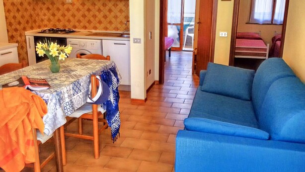 Un espace de vie compact comprenant un coin repas, une kitchenette et un canapé bleu.
