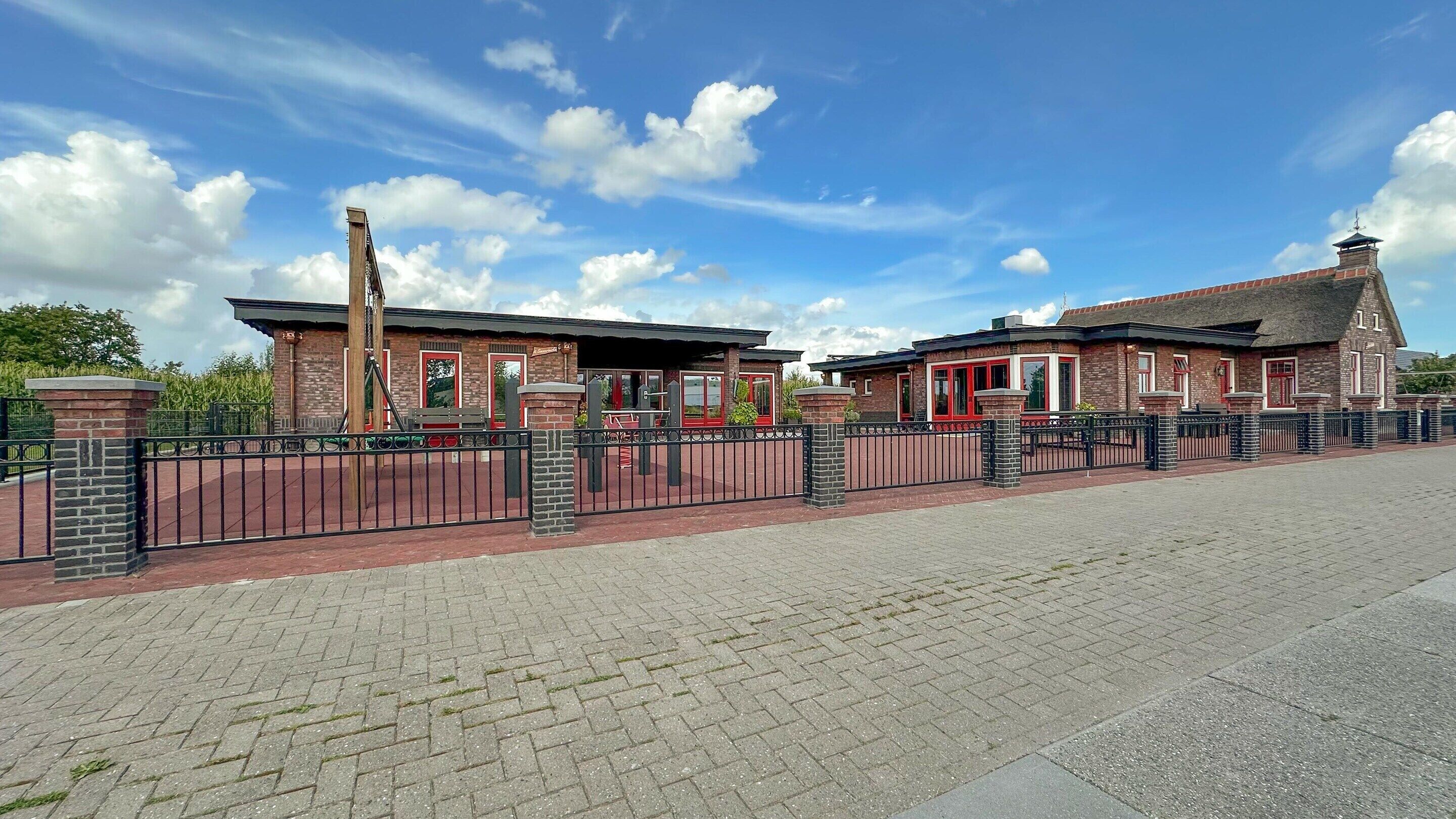 Ein Gebäude aus Ziegelsteinen mit roter Tür und Schornstein, umzäunt durch einen schwarzen Metallzaun.