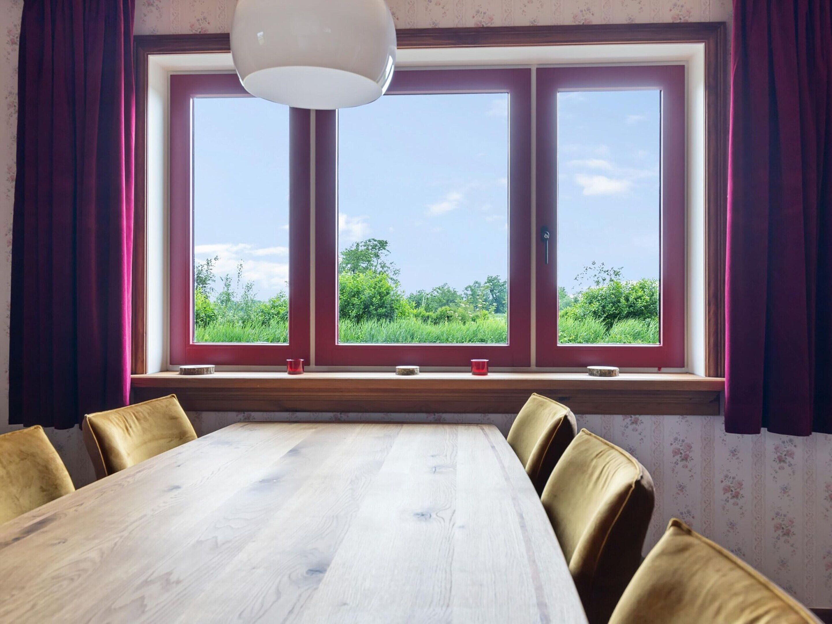 Un coin repas avec une grande table en bois et six chaises, une fenêtre donnant sur un paysage verdoyant et un luminaire suspendu.