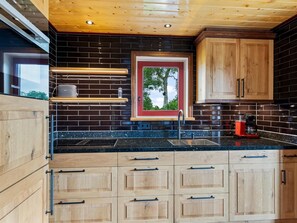 A modern kitchen with wooden cabinets, a black countertop, and a window with a red frame. - Holiday Home in Friesland Near Canal & Lake (Jistrum)
