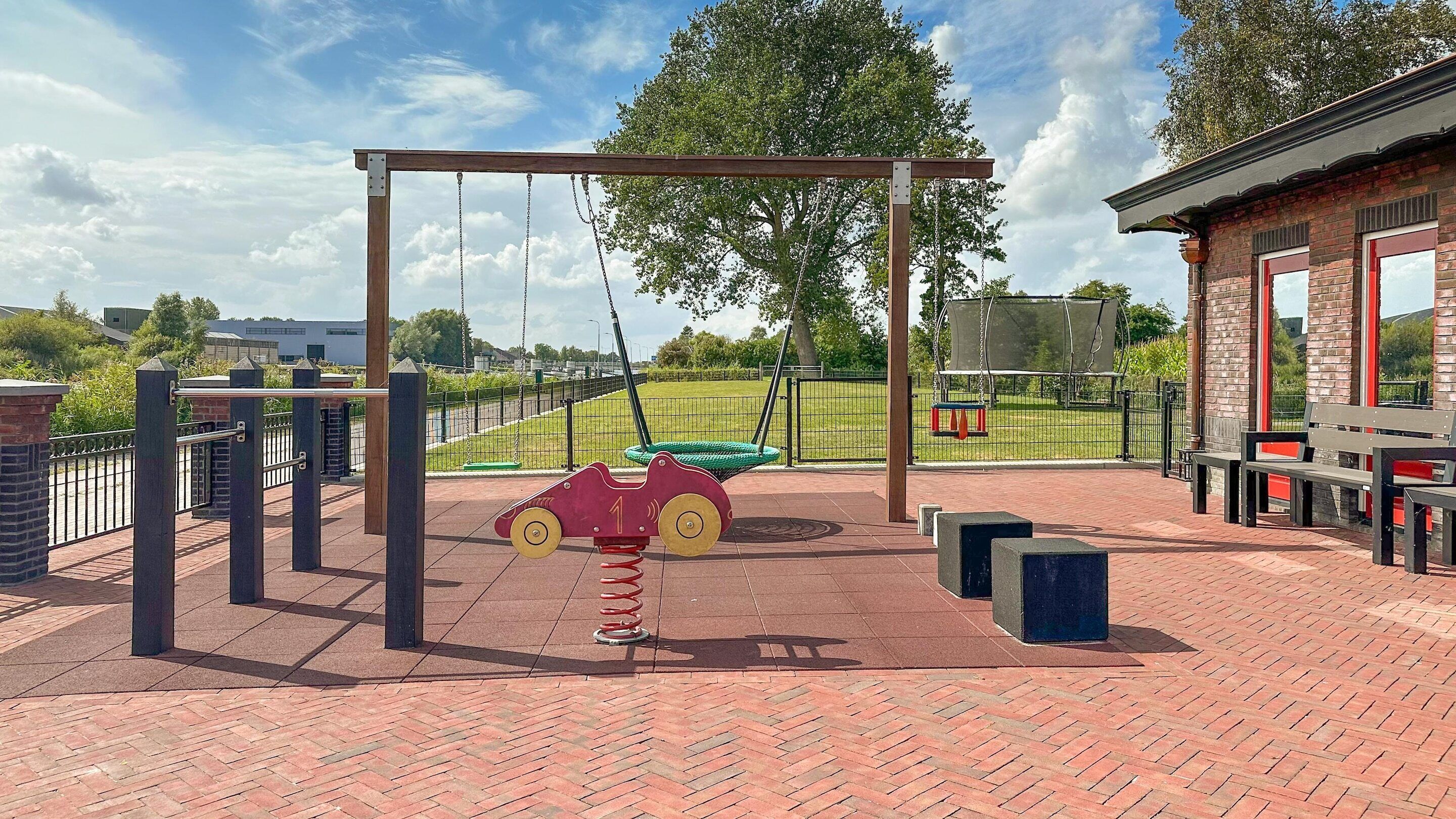Ein Spielplatz mit Schaukeln, einer roten Autoschaukel und einem von Ziegelsteinen gepflasterten Bereich.