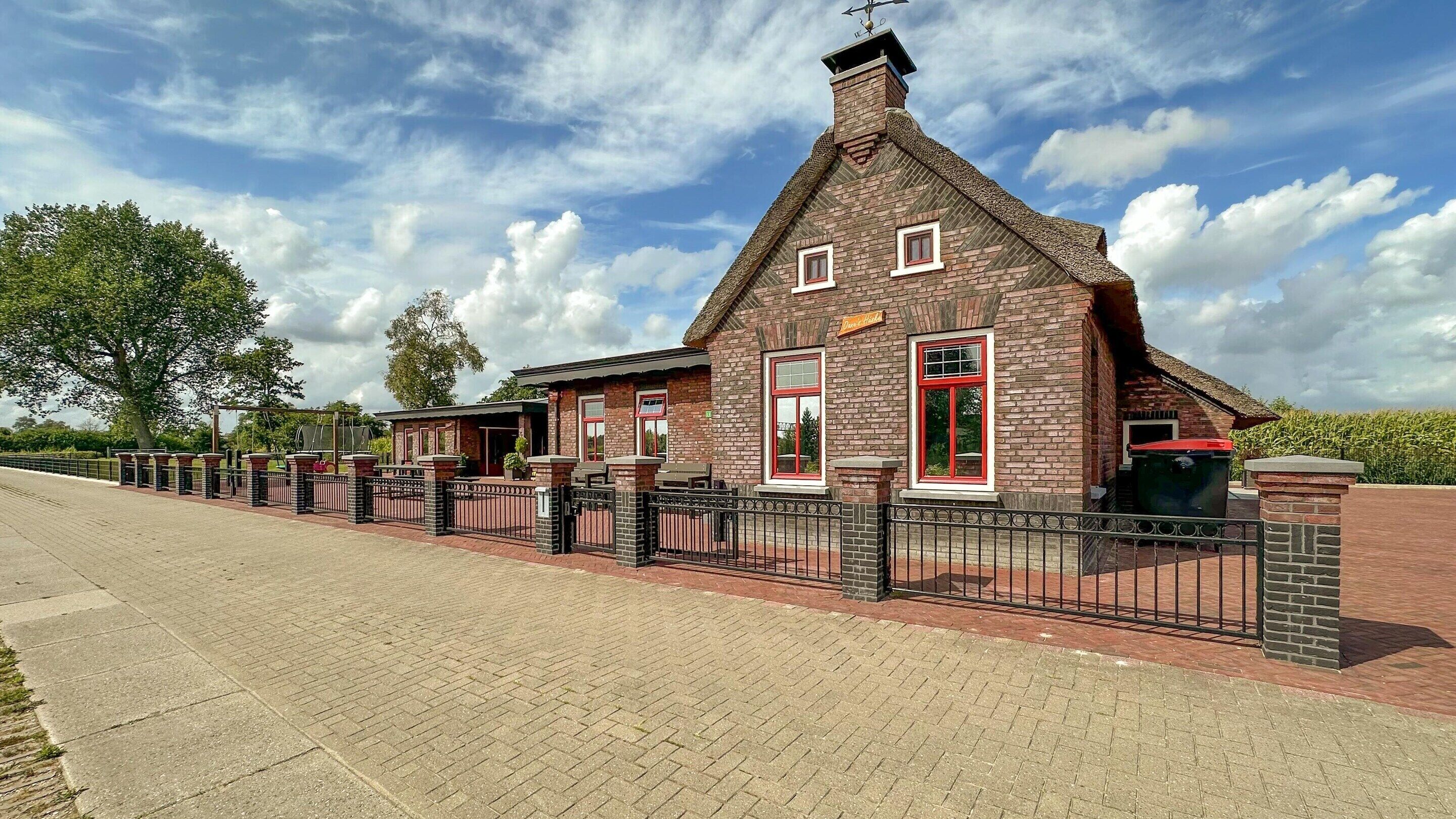 A brick building with a red door and windows, a sign above the door, and a fence in front.
