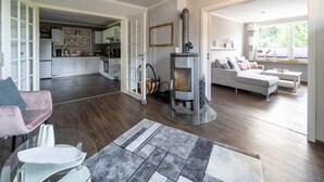 Amplia sala de estar con chimenea, cocina al fondo y un rincón de descanso acogedor con sofá y mesa de centro.