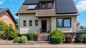 Una casa de dos plantas con techo inclinado, paneles solares y fachada de ladrillo.