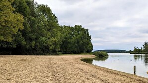A sandy beach with a calm lake, surrounded by dense trees. - Holiday Home in South Holland Near Rotterdam (Simonshaven)