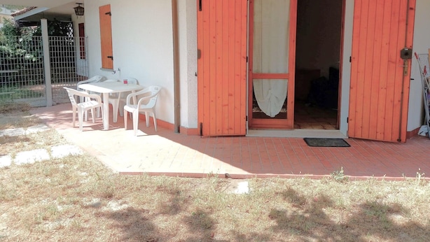 A patio with a table and chairs, a red door, and a small garden area. - Attractive Villa With Garden (Ravenna)