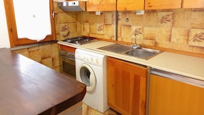 A compact kitchen with wooden cabinets, a gas stove, a built-in oven, a washing machine, and a sink. - Attractive Villa With Garden (Ravenna)