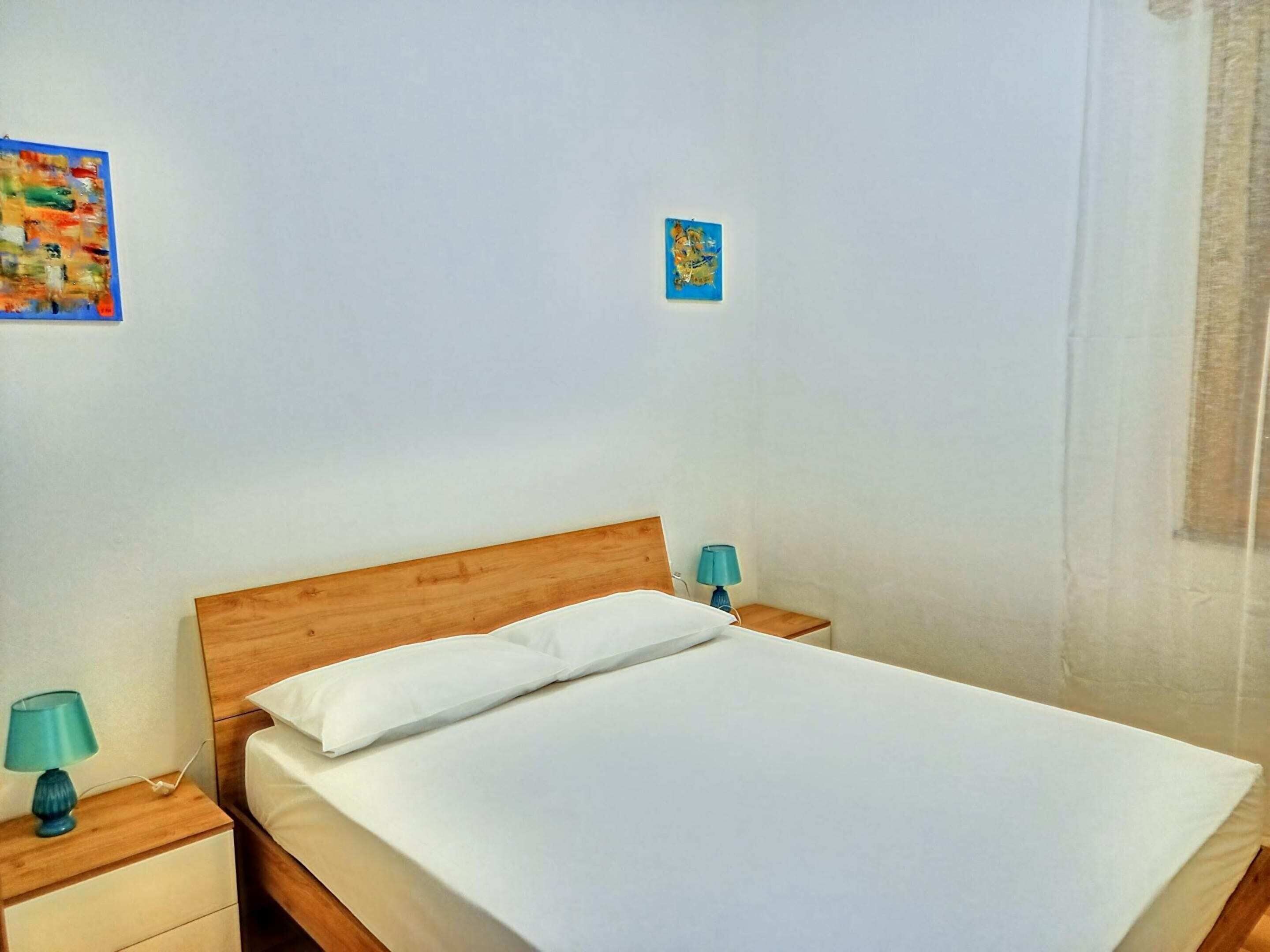 Un letto rifatto con cura in una camera d'albergo, con una testiera in legno, due comodini con lampade e un piccolo oggetto decorativo al muro.