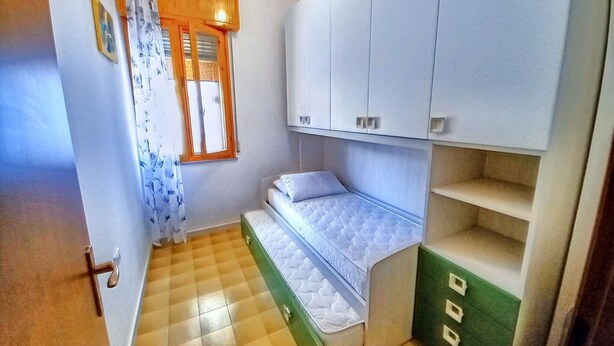 A compact room with a bed, a small window with curtains, and a wardrobe. - Cosy Apartment With Balcony (Ravenna)