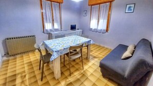 A small, well-lit room with a dining table, two chairs, a sofa, and a computer on a desk. - Cosy Apartment With Balcony (Ravenna)