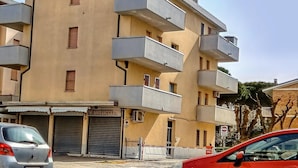 A multi-story residential building with balconies, a closed shop, and parked cars. - Cosy Apartment With Balcony (Ravenna)