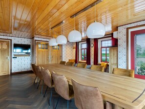 Un vaste espace dédié à la salle à manger, avec une longue table en bois et de nombreuses chaises, un plafond en bois et de grandes fenêtres dotées de rideaux.