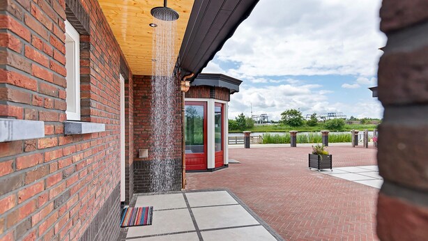 Un bâtiment en briques agrémenté d’un élément décoratif aquatique, d’une porte rouge et d’une zone pavée avec des jardinières.