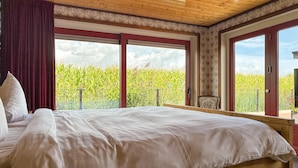 Une chambre avec un grand lit, une vue sur un champ de maïs par une porte coulissante et un balcon avec une chaise.