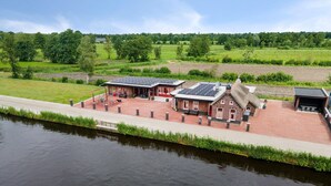 Un bâtiment situé au bord de la rivière, doté de panneaux solaires, d’une façade en briques rouges et d’un toit de chaume.