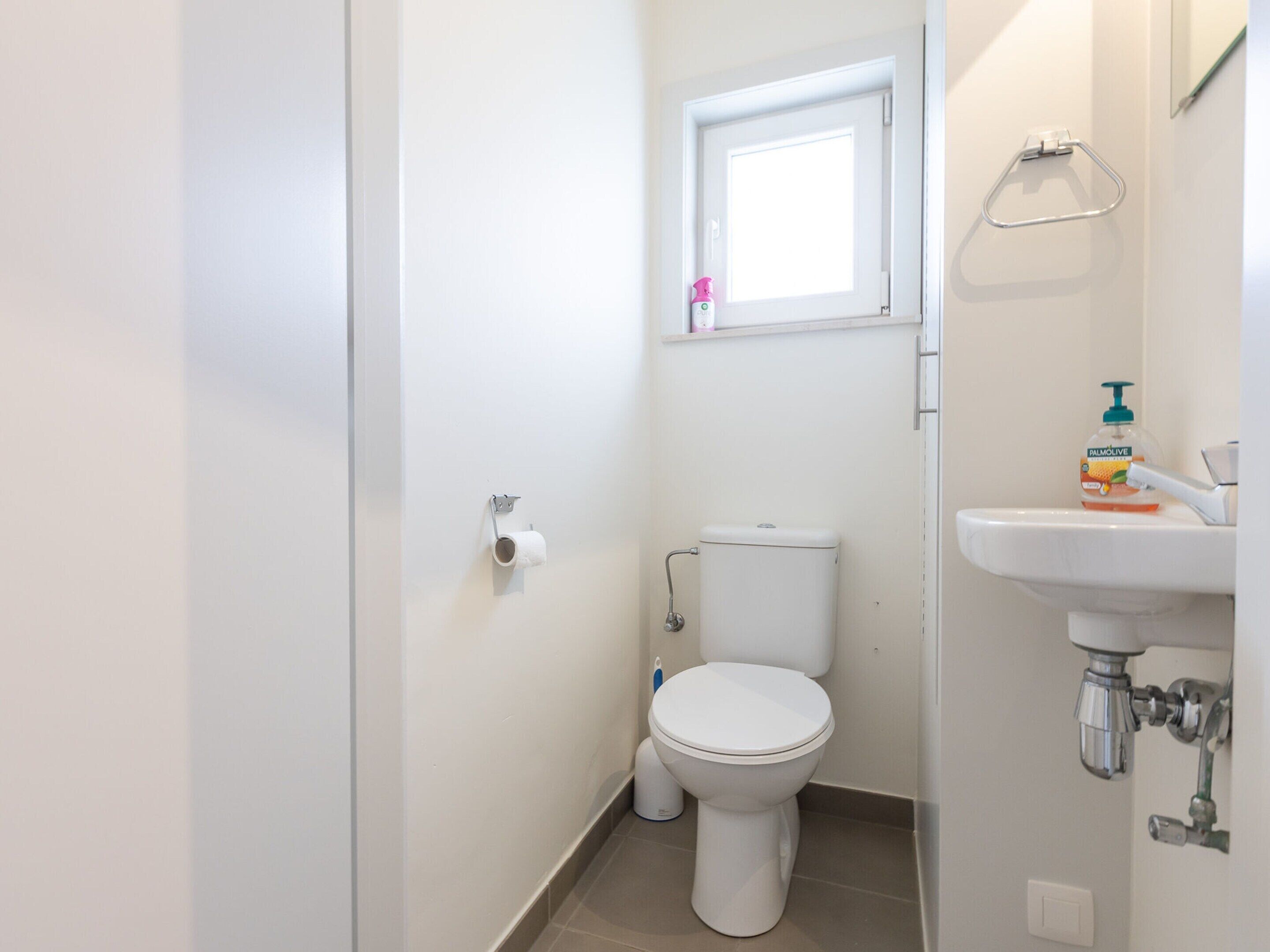 Een kleine, schone badkamer met toilet, raam en wastafel.
