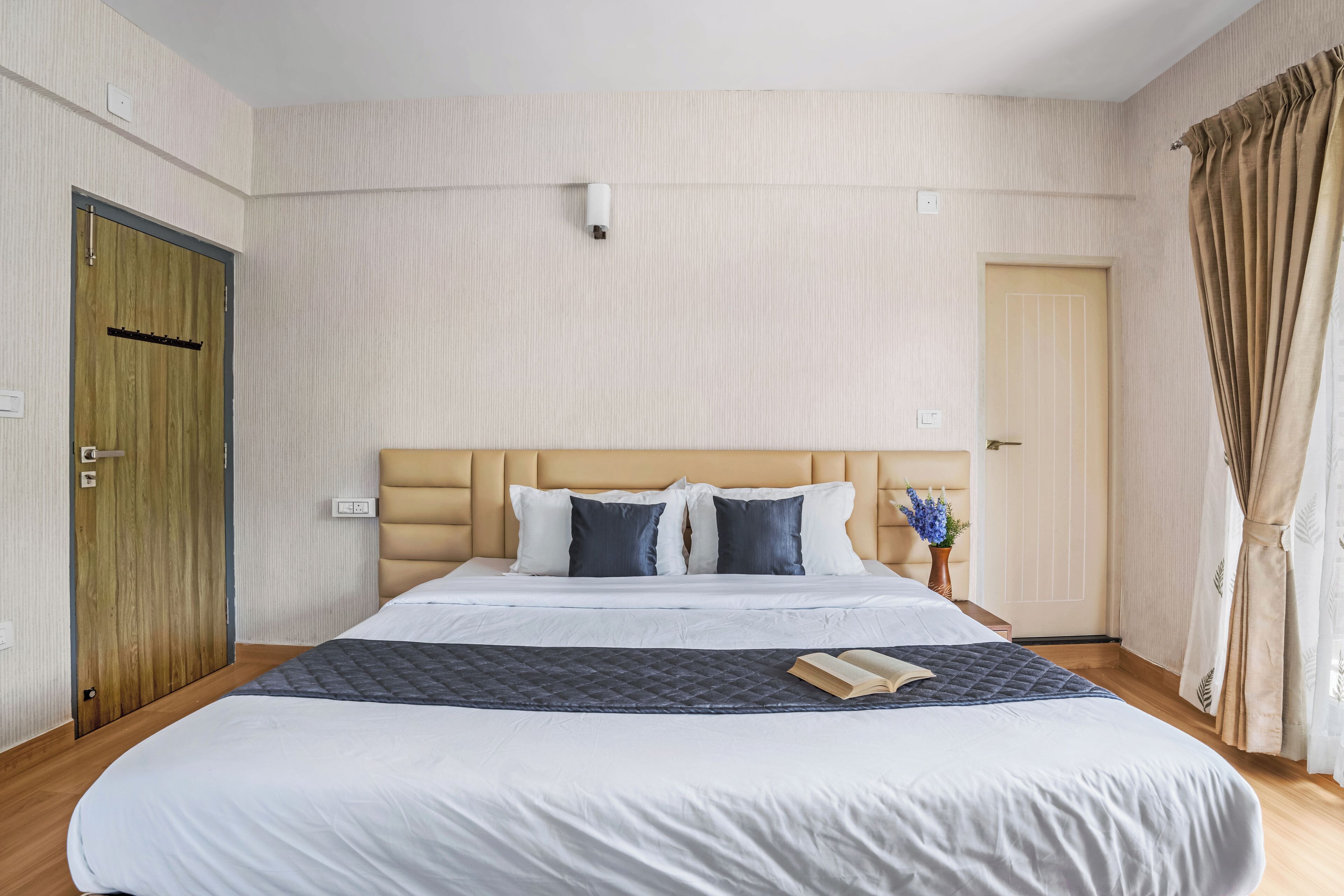 Habitación de hotel impecable con una cama grande, una mesita de noche con un florero y una puerta de madera.