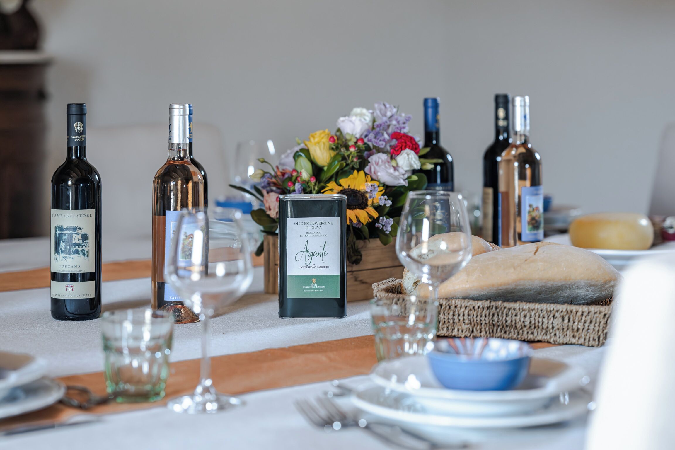 Uma mesa posta com garrafas de vinho, copos, um arranjo floral e uma baguete.