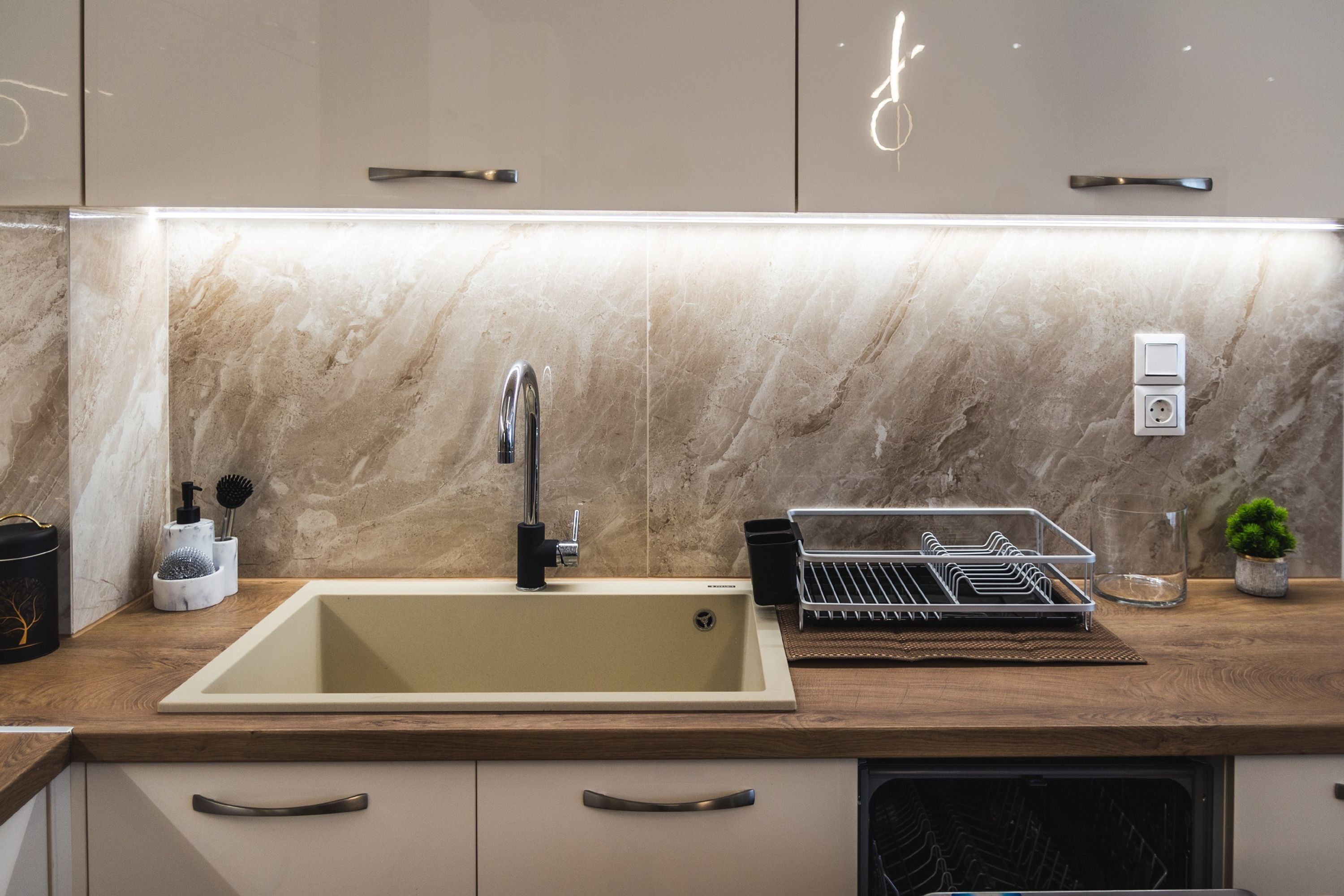 A modern kitchen with a marble backsplash, a sink with a faucet, and a dish drying rack.