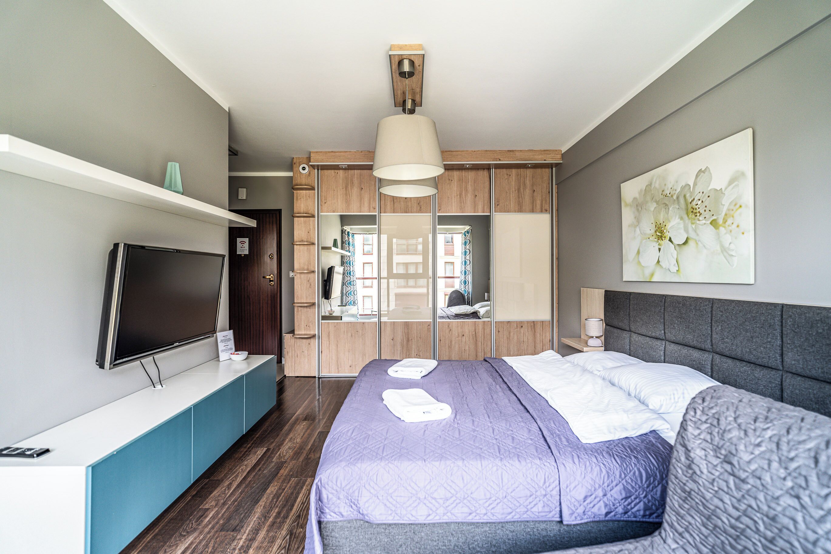 A modern hotel room with a large bed, a flat-screen TV, a mirror, and a painting on the wall.