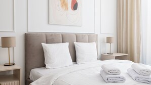 Ein ordentlich eingerichtetes Hotelzimmer mit einem großen Bett, zwei Nachttischen mit Lampen, einem modernen Wandbild und einem Fenster mit Vorhängen.