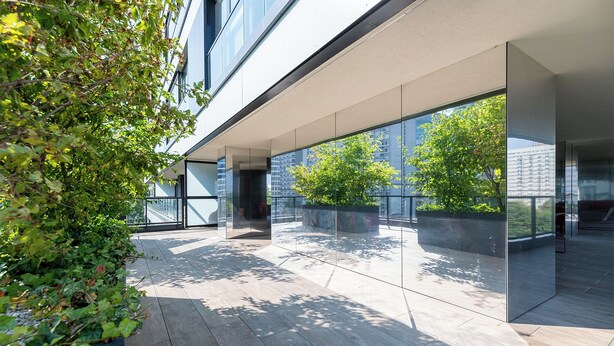 Ein modernes Gebäude mit großen Glasfenstern, einer flachen Dachkonstruktion und einer Holzterrasse.