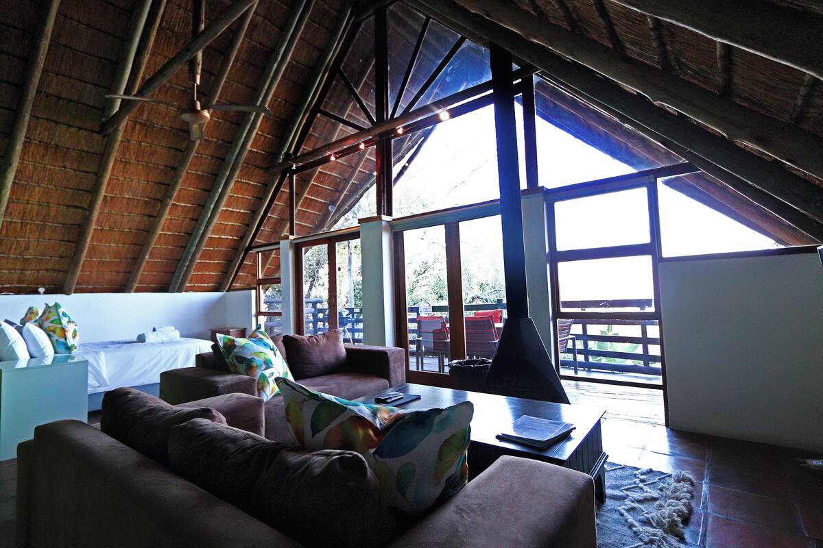 Una habitación acogedora con techo inclinado, una cama, un sofá y una mesa con una lámpara.