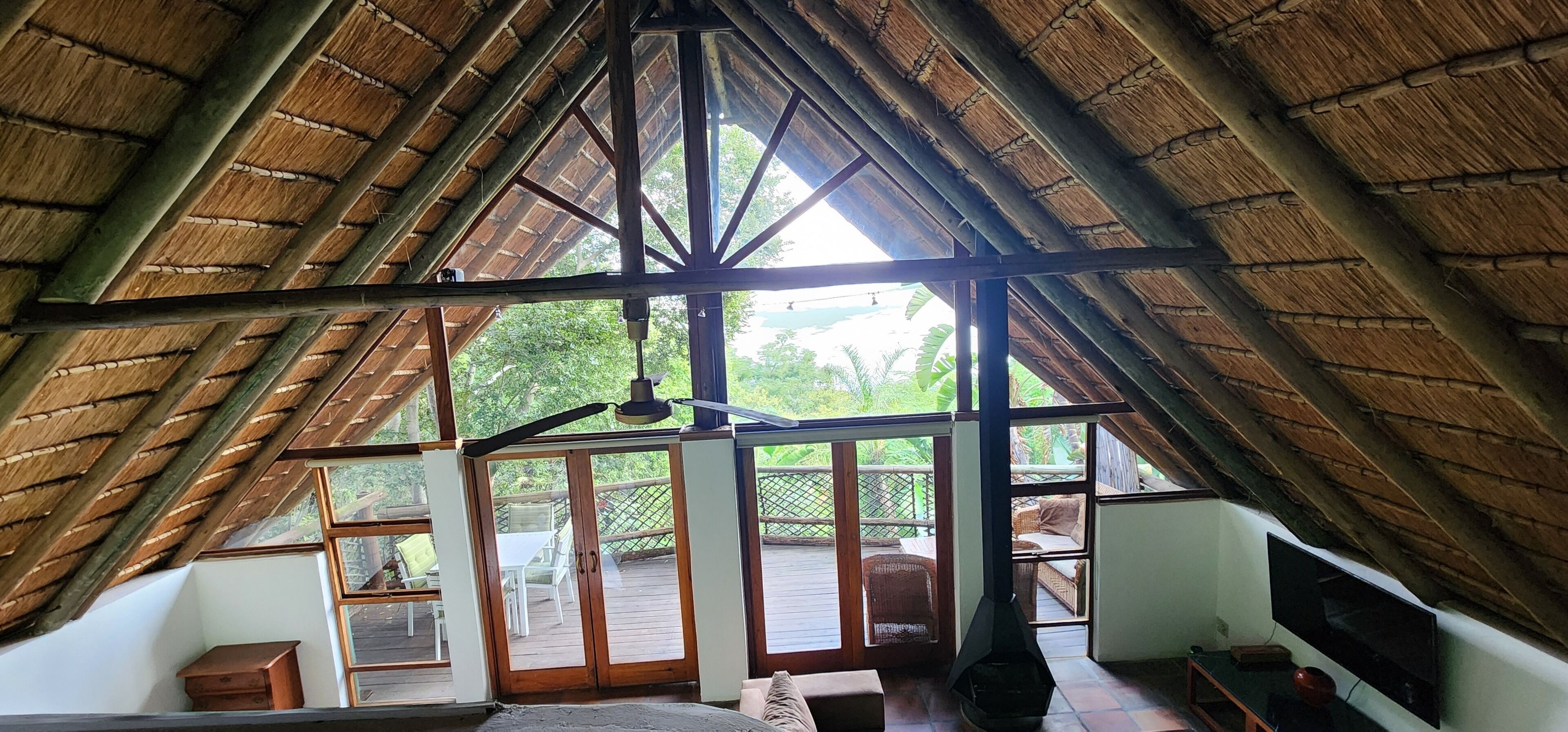 A high-ceilinged room with a thatched roof, large windows, and a view of an outdoor deck.