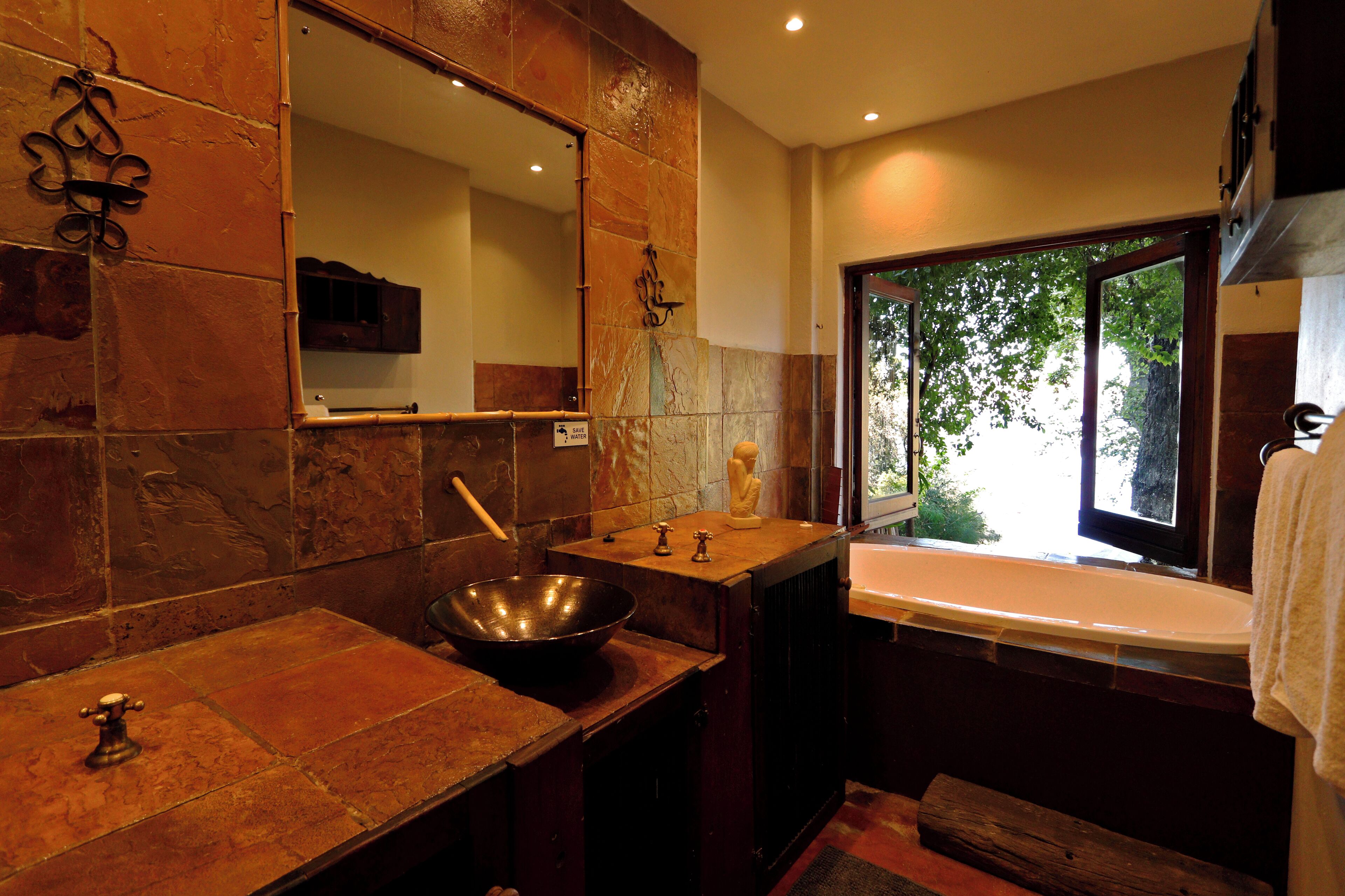 A bathroom with a large mirror, a sink with a bowl, a window with a view of trees, and a towel hanging on the wall.