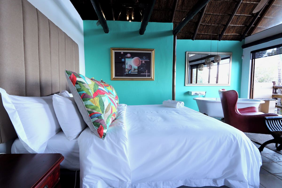 Una habitación de hotel con una cama, una silla, una mesita, un espejo y una ventana.