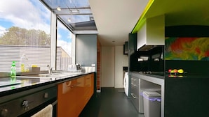 A modern kitchen with a large window, a washing machine, and a colorful abstract painting.