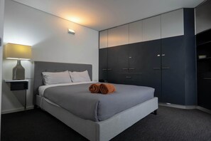 A modern hotel room with a bed, bedside table, lamp, and built-in wardrobe.