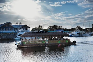 A boat with a thatched roof and 'Tiki Taka Cruises' branding, docked at a marina with other boats and a building in the background. - Sailfish Suites 1 - Waterfront & pet friendly! (Stuart)