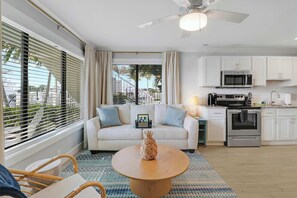 A modern living room with a sofa, a round coffee table, and a kitchen area with white cabinets and appliances. - Sailfish Suites 1 - Waterfront & pet friendly! (Stuart)