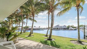 A patio with white chairs, palm trees, and a view of a marina with boats. - Sailfish Suites 1 - Waterfront & pet friendly! (Stuart)