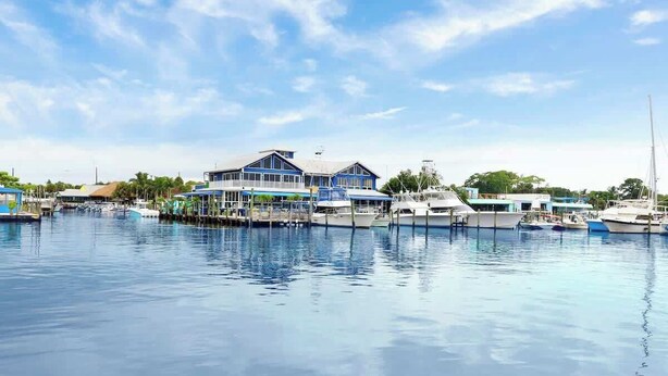 A marina with several boats docked, a large building with a blue roof, and a clear sky. - Sailfish Suites 1 - Waterfront & pet friendly! (Stuart)