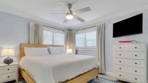 A bedroom with a bed, a nightstand, a dresser, a ceiling fan, a TV, and two windows with curtains. - Sailfish Suites 1 - Waterfront & pet friendly! (Stuart)