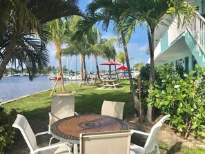 A patio with a round table and chairs, surrounded by palm trees and a view of the water.