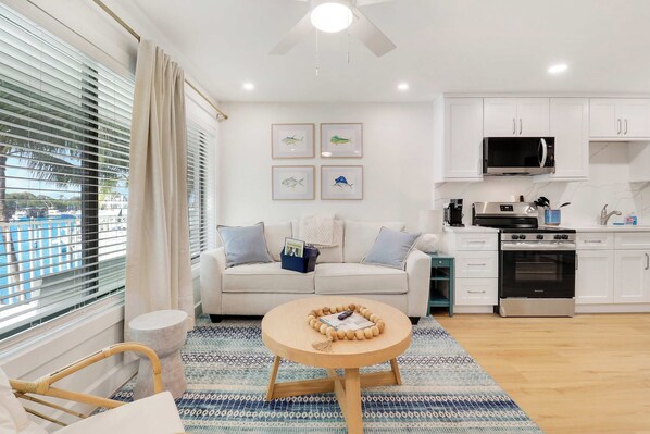 A modern living room with a sofa, a coffee table, and a kitchen area with a microwave and stove. - Sailfish Suites 2 - pet friendly & waterfront!!! (Stuart)
