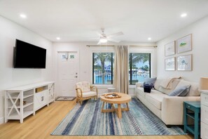 A living room with a flat-screen TV, a white sofa, a wicker chair, a round wooden coffee table, and a blue patterned rug. - Sailfish Suites 2 - pet friendly & waterfront!!! (Stuart)