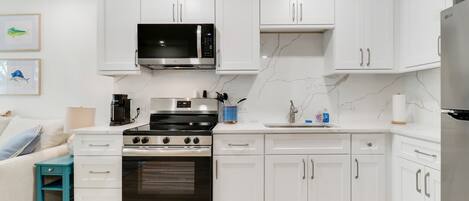 A modern kitchen with white cabinetry, a stainless steel refrigerator, an oven, a microwave, and a coffee maker.