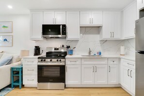 A modern kitchen with white cabinetry, a stainless steel refrigerator, an oven, a microwave, and a coffee maker. - Sailfish Suites 2 - pet friendly & waterfront!!! (Stuart)