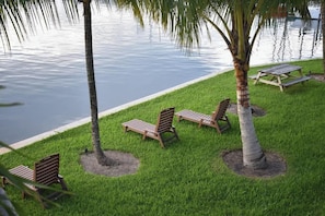 A serene outdoor seating area with wooden loungers and palm trees by a calm body of water.