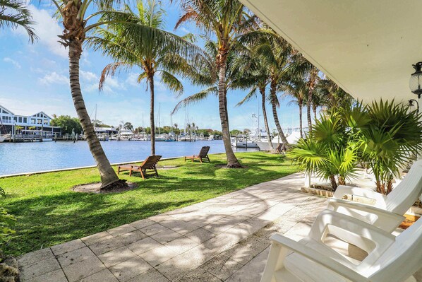 A waterfront patio with lounge chairs, palm trees, and a marina in the background.