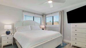A bedroom with a bed, nightstands, a dresser, a TV, and a ceiling fan. - Sailfish Suites 7 - Waterfront Lodging (Stuart)