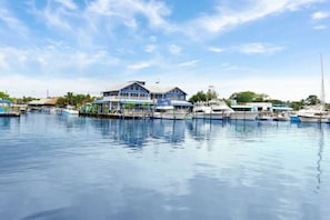 A marina with boats docked, a large building with a blue roof, and a clear sky.