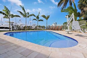 Une piscine à bord incurvé, entourée de palmiers et d’une clôture blanche.